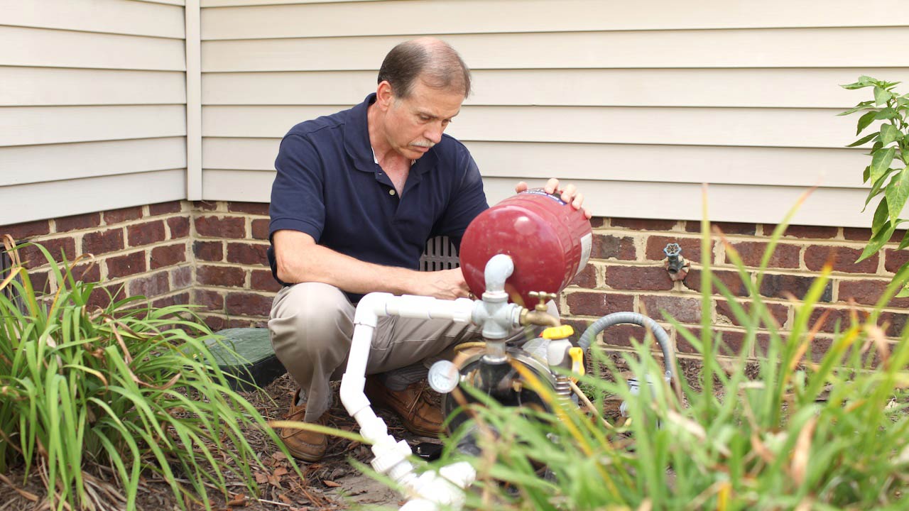 Man performs routine maintenance on home well pump outside house