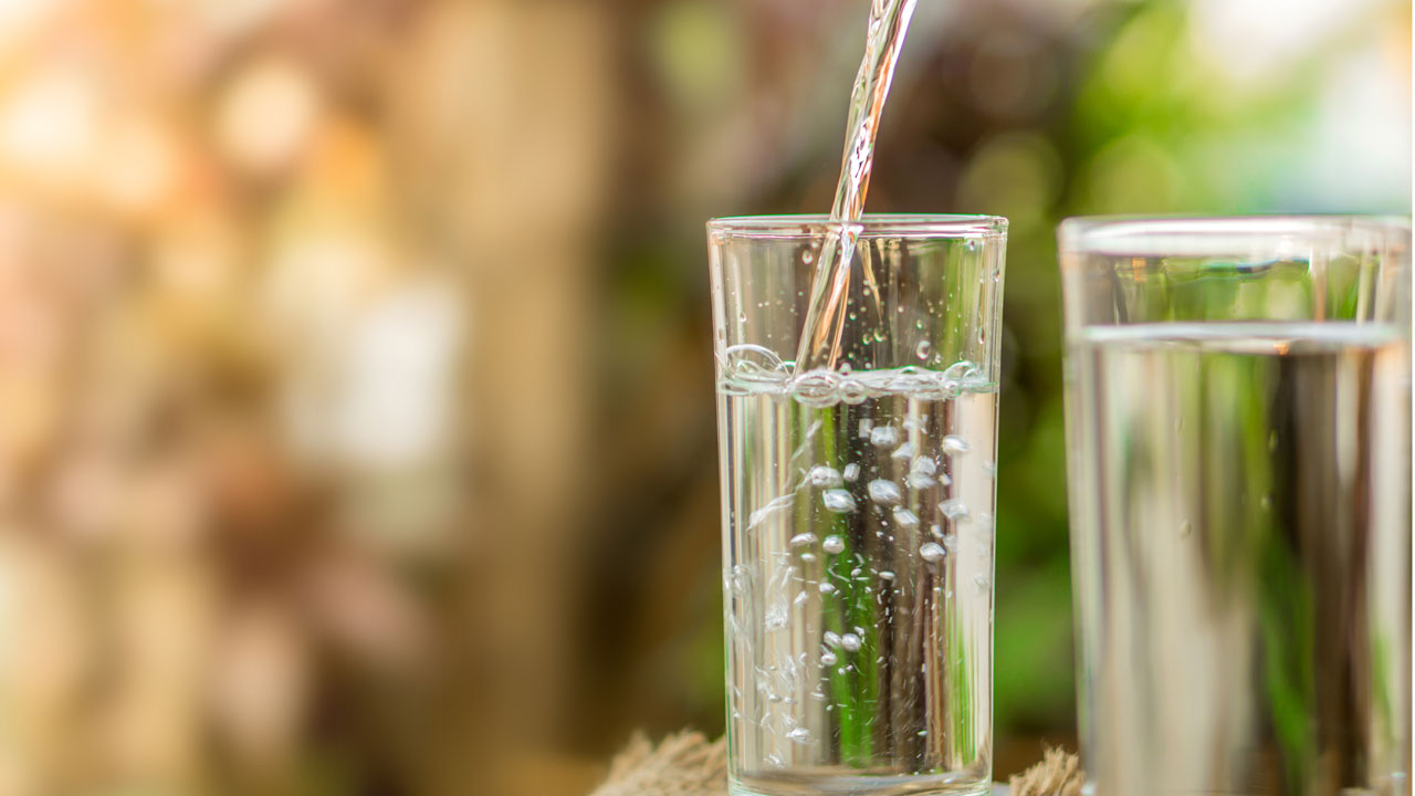 Purified water filling a glass against a natural backdrop