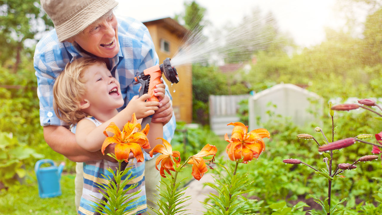 Grandfather and child in a garden with a garden hose spraying at high pressure.