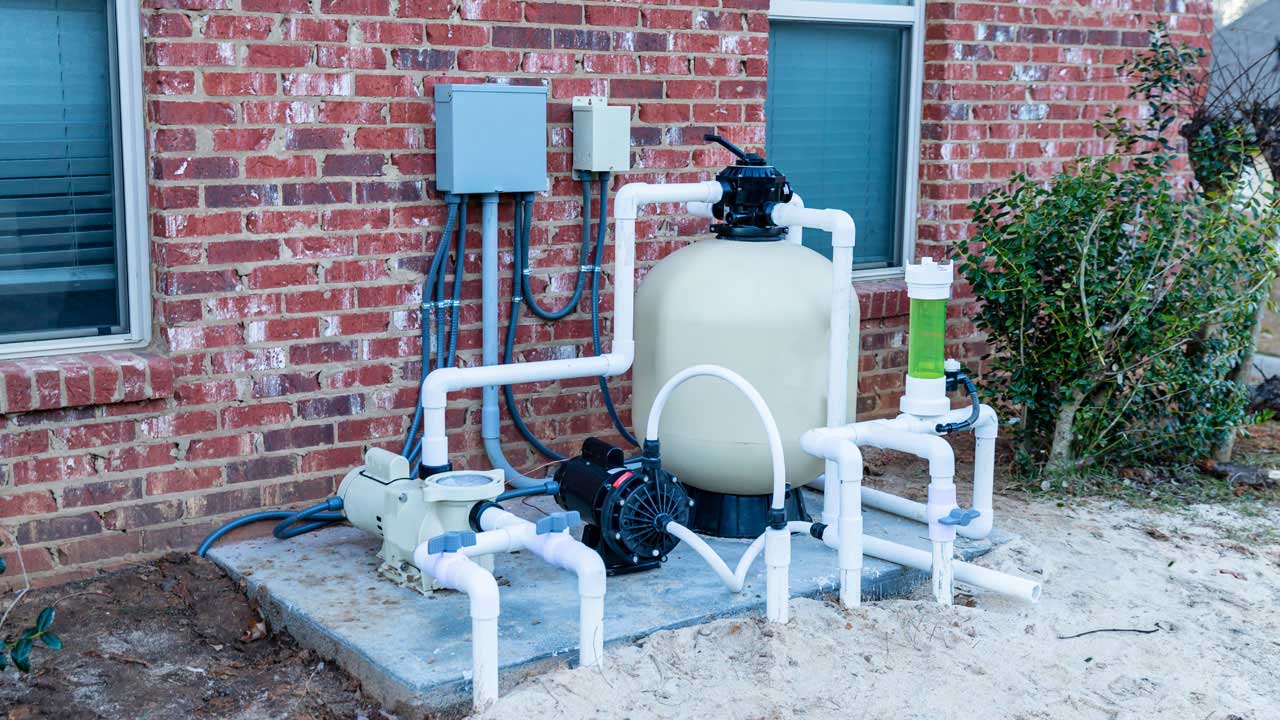 A large white pool sand filter with white PVC plumbing and a pool pump connected to residential electric.
