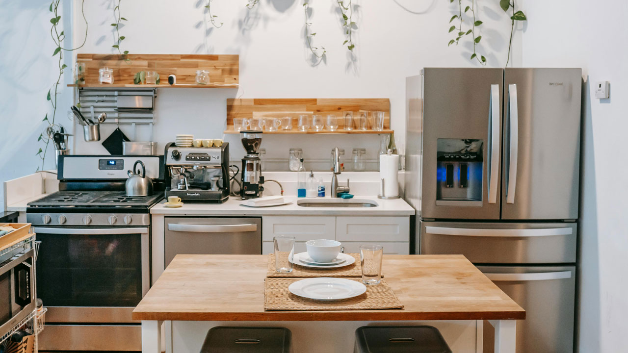 A clean, modern kitchen with a white wall and a contemporary stainless steel refrigerator with water dispenser. Pexel photo by Charlotte May.