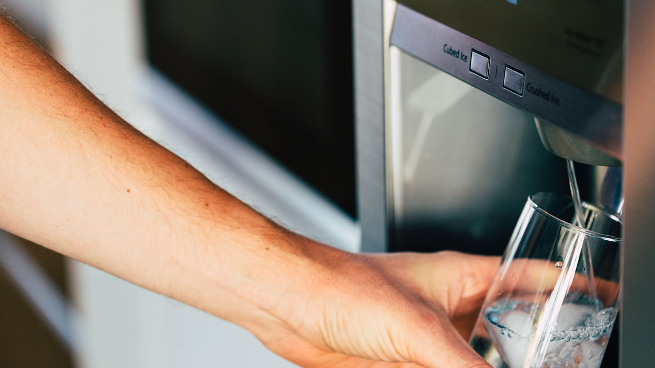 Hand holding a glass to a water filter dispenser