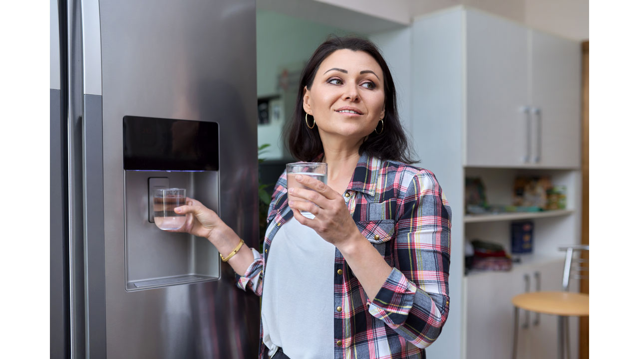 Woman filling two water glasses at refrigerator water dispenser
