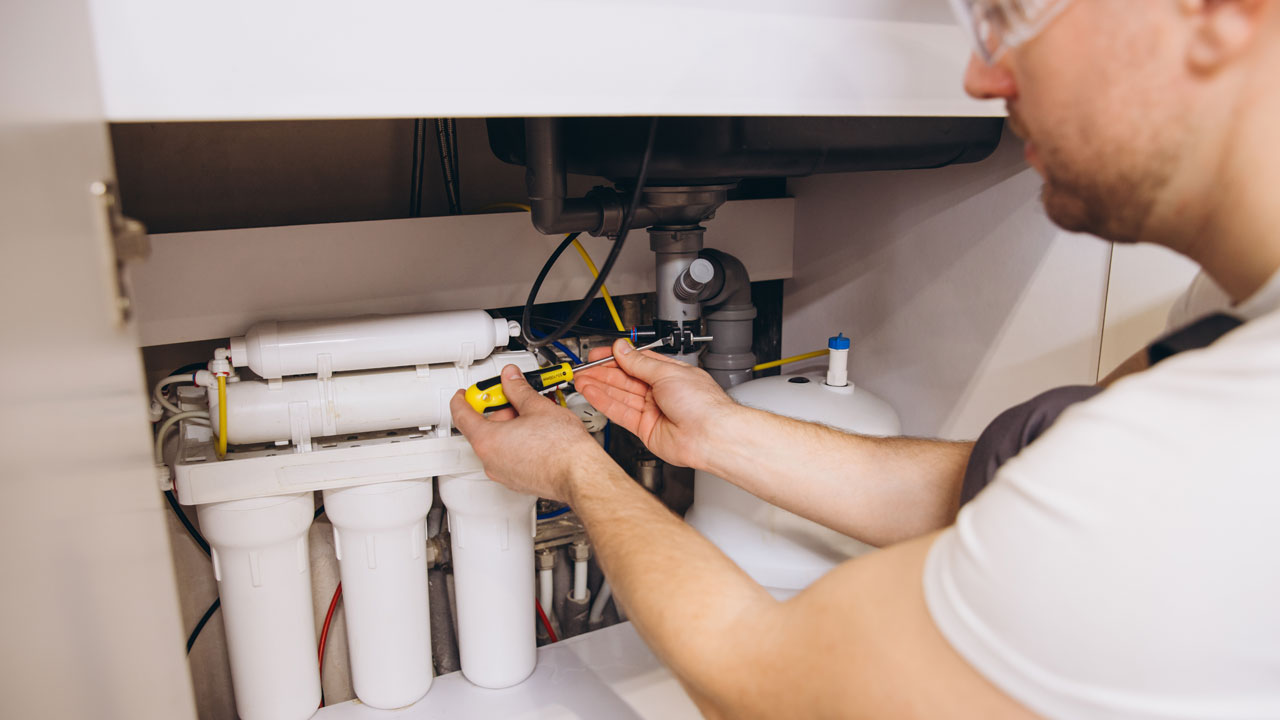 Plumber or home DIYer with screwdriver installing drain saddle for under sink reverse osmosis