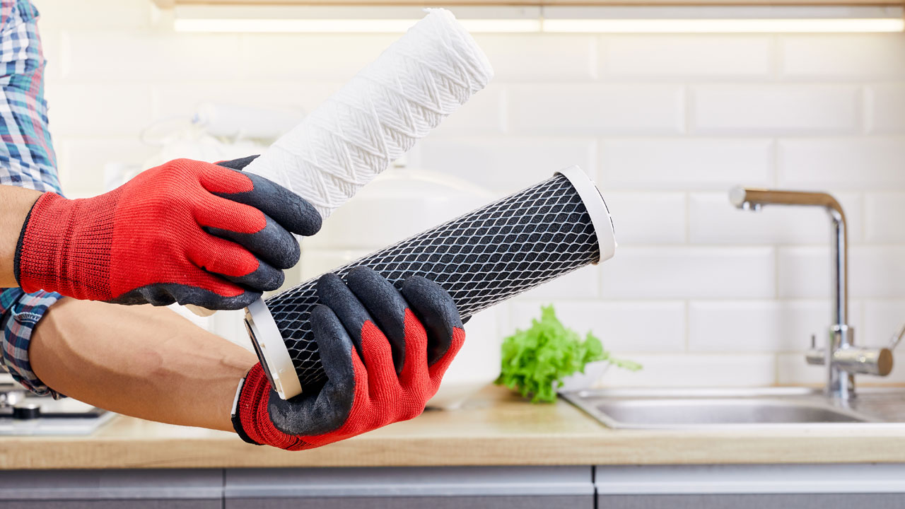 Gloved hand holding a sediment and carbon filter for replacing