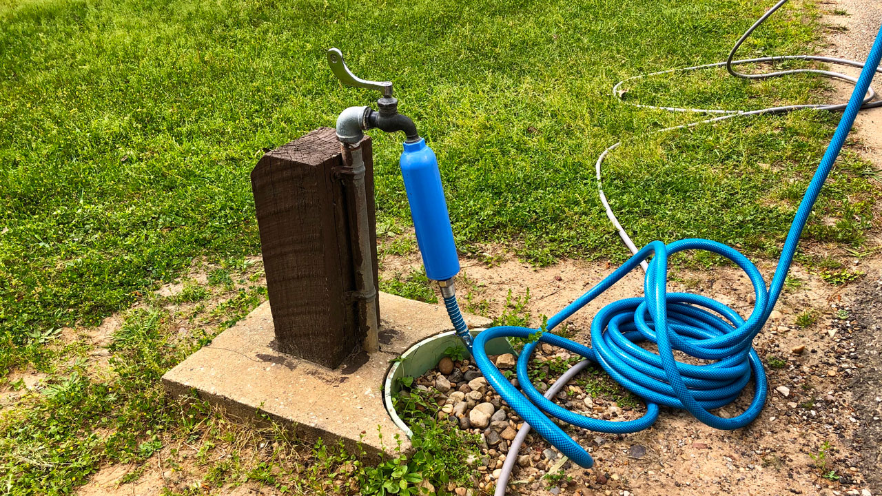 A blue inline water filter attached to a campground spigot with hose running toward RV