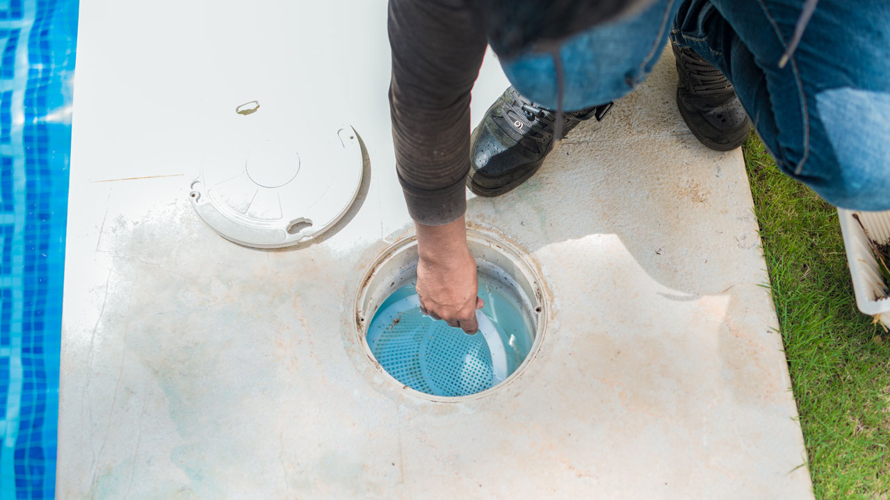 A hand pulling a skimmer basket out where fresh DE powder is added to replenish DE pool filter grids.