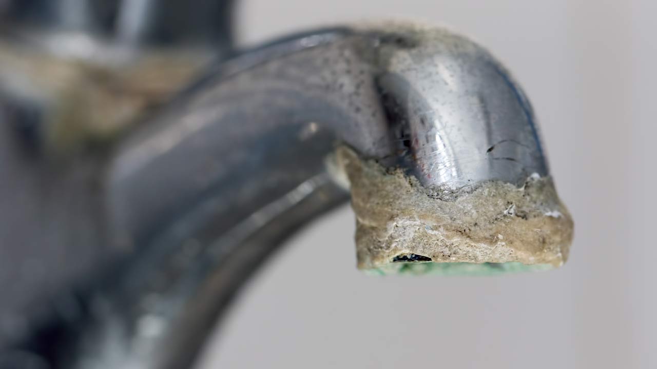 Stainless steel faucet crusted in hard water mineral buildup