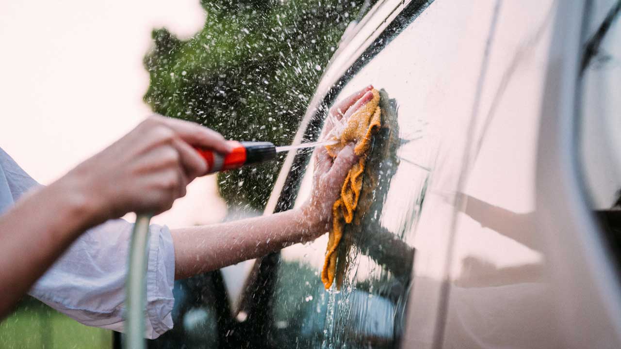 A hose attachment spraying spot-free reverse osmosis water on a car