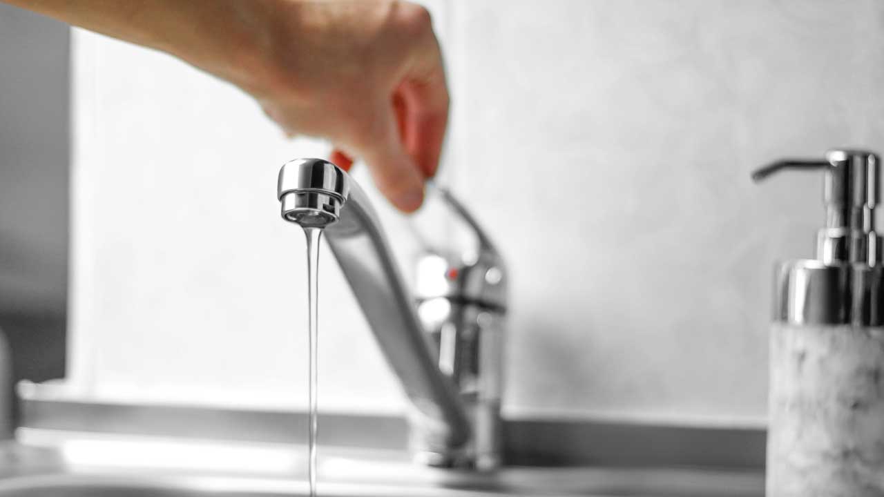 A hand turns on a kitchen faucet where drinking and cooking water is used
