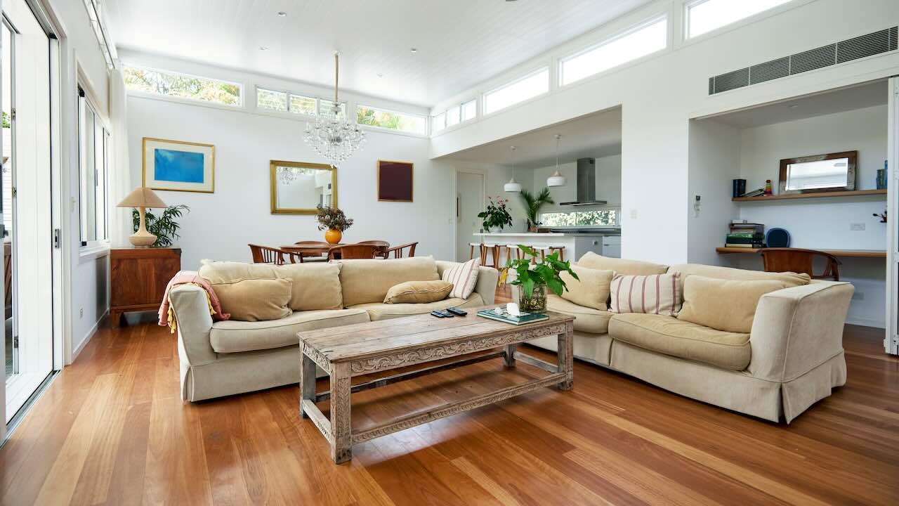 A large bright living area with couch and shelves and a long air vent near the ceiling