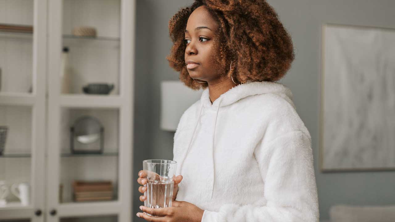 Woman in white hoody holding tall, clear glass of water