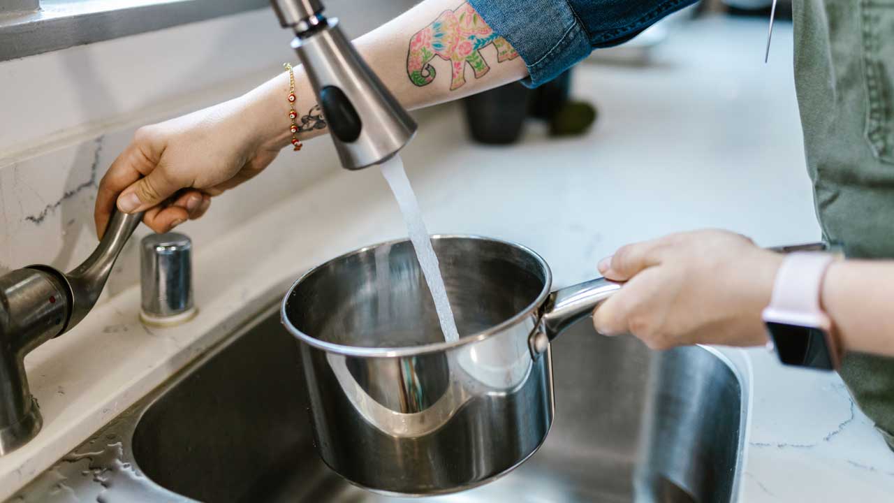 Adult hands filling a pot with tap water in a kitchen sink. Pexels photo: RDNE Stock Project