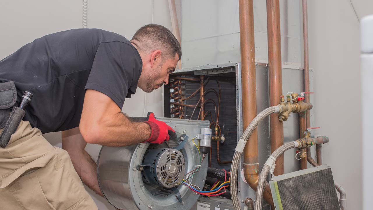 HVAC man with a plan with red service gloves handling a large metal blower motor inside a furnace cabinet
