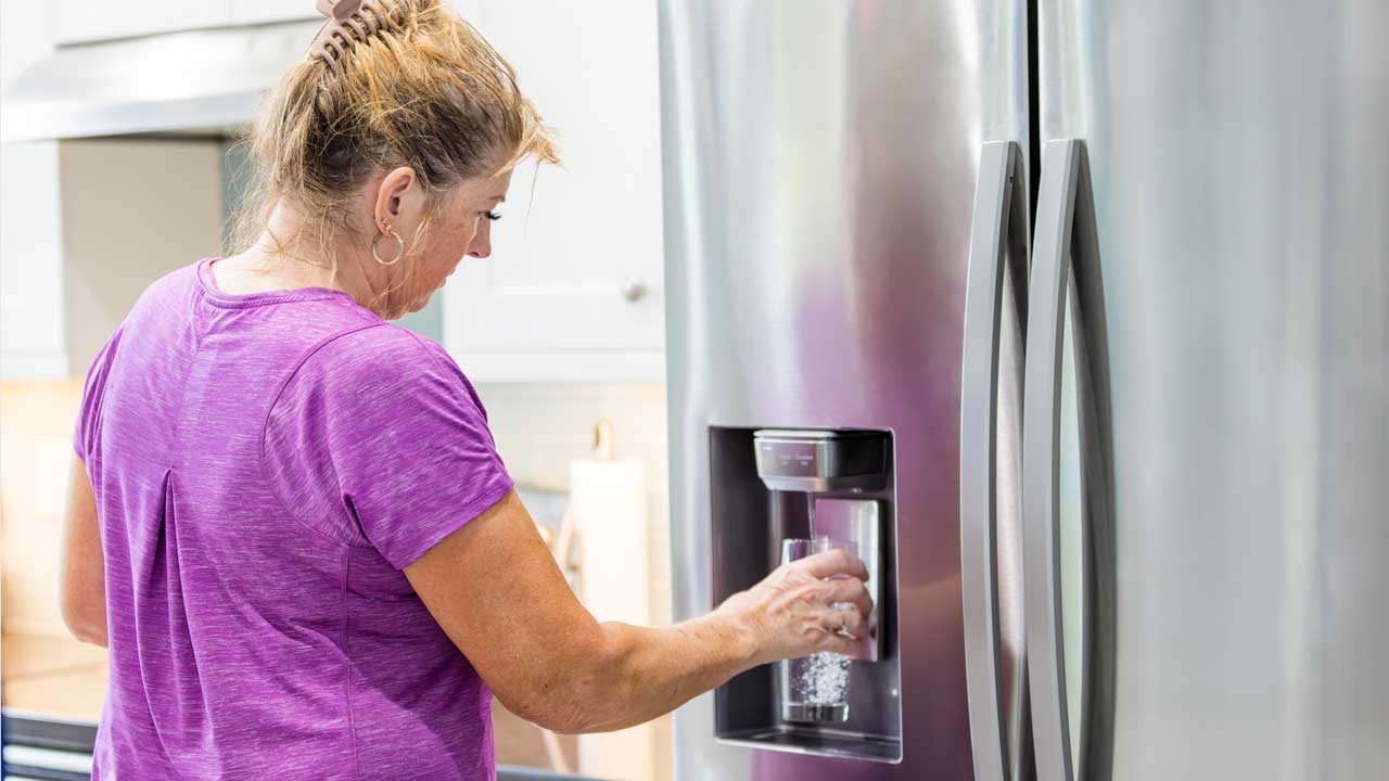 Woman at a refrigerator getting water and ice from a dispenser after a refrigerator water filter