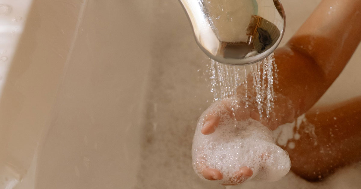 A small hand filled with soapy lather from soft water in a bathtub