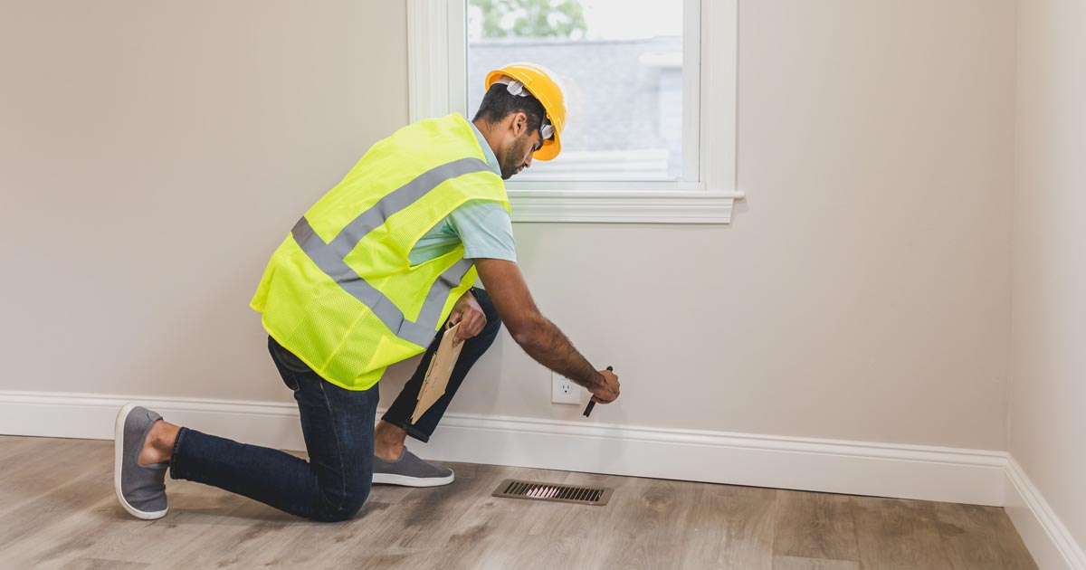 Male inspector in bright vest shining flashlight into an HVAC floor vent