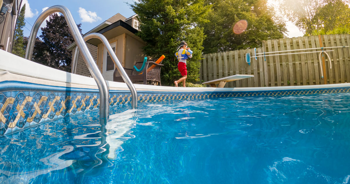 Clean blue pool water in foreground with a child in a personal floatation device walking along the side of the pool.