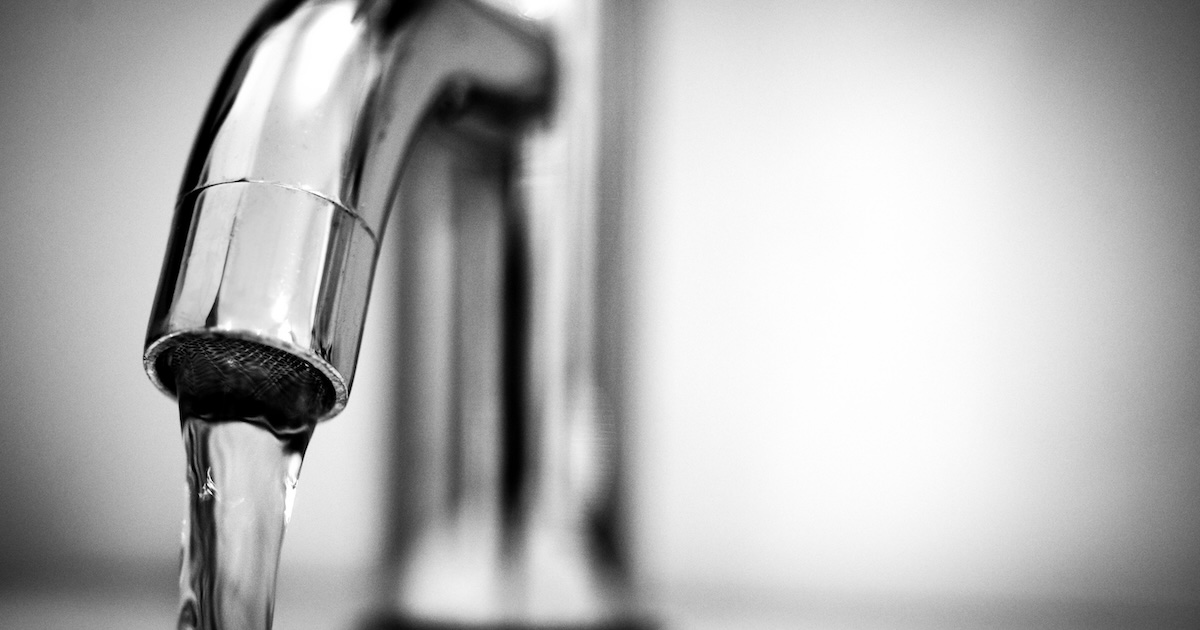 A close-up photograph of a running water faucet in a sink
