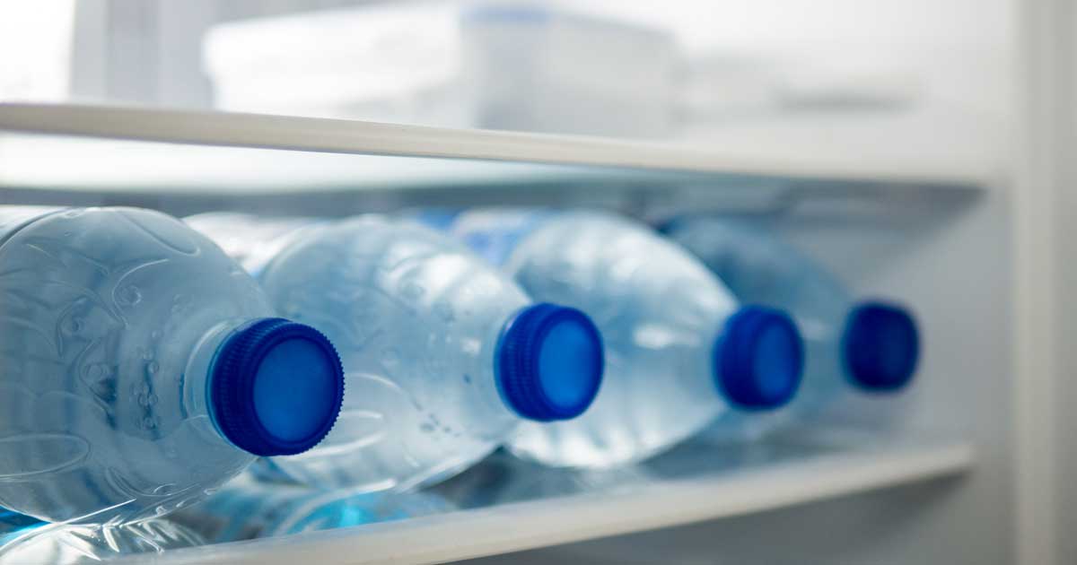 Four blue plastic single-serve plastic water bottles on their side on a shelf in a refrigerator