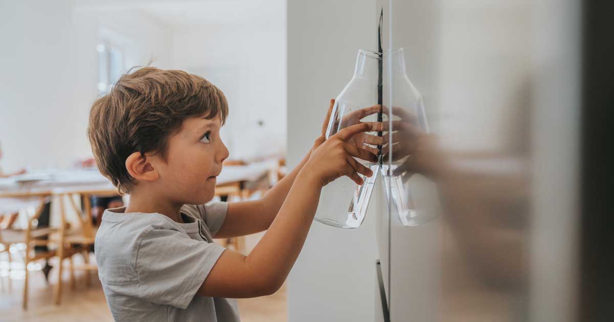 Boy with glass carafe refilling water from refrigerator water and ice dispenser