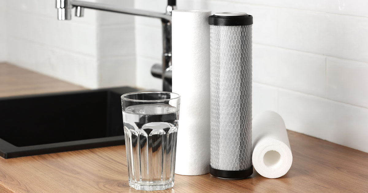 A white polypropylene sediment filter and a black and white carbon filter next to a glass of water